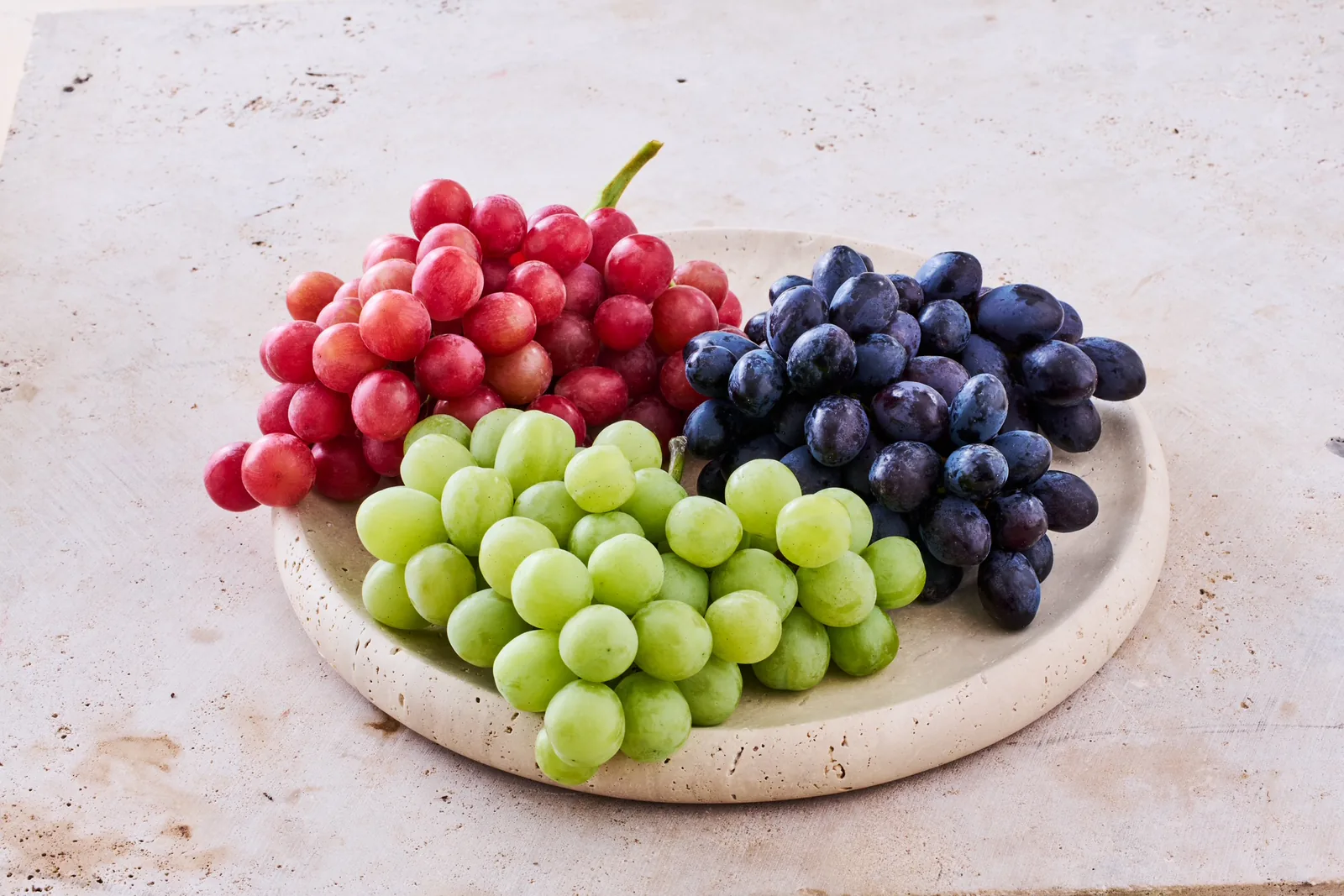 Green, red and black California table grapes arranged on a serving plate.